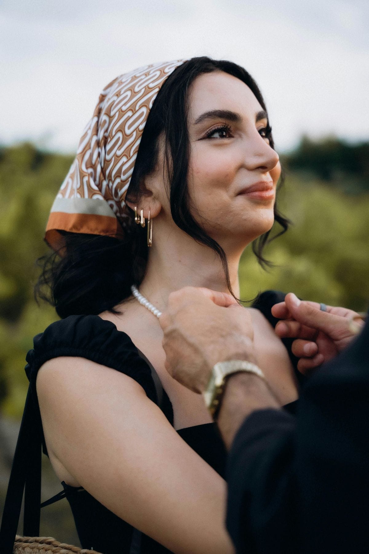 Couple adjusting pearl necklace outdoors, showcasing affection and style