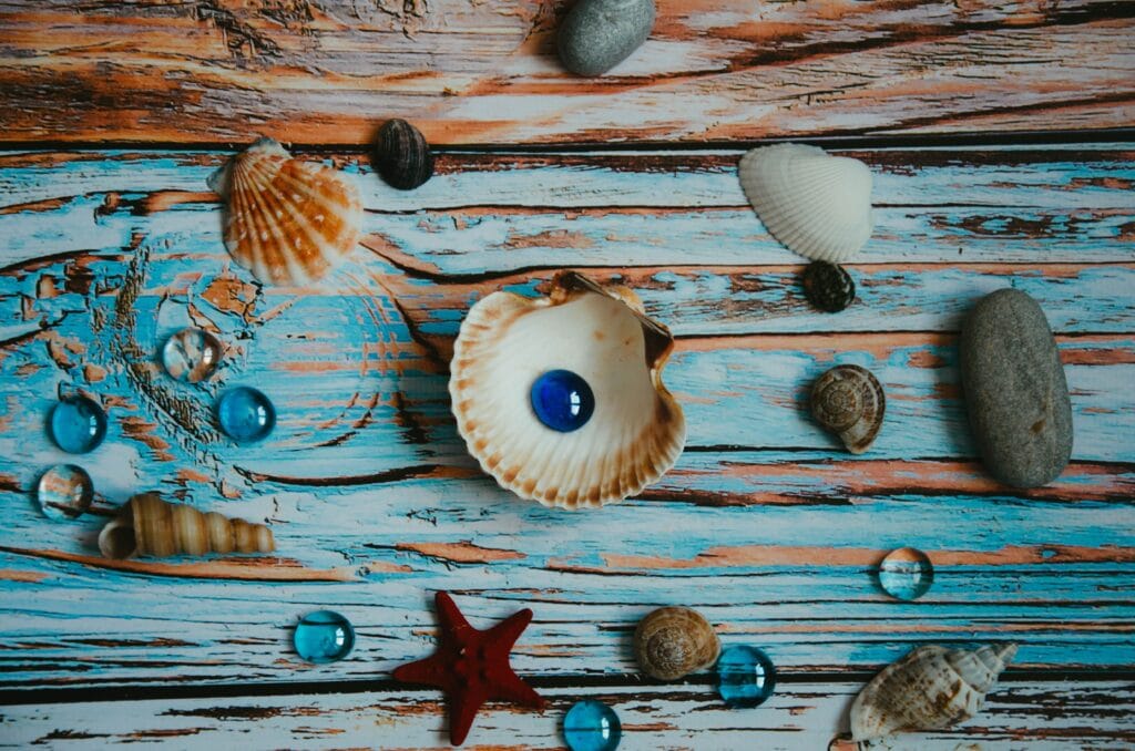 A colorful flat lay of seashells, stones, and glass beads on weathered wooden planks.