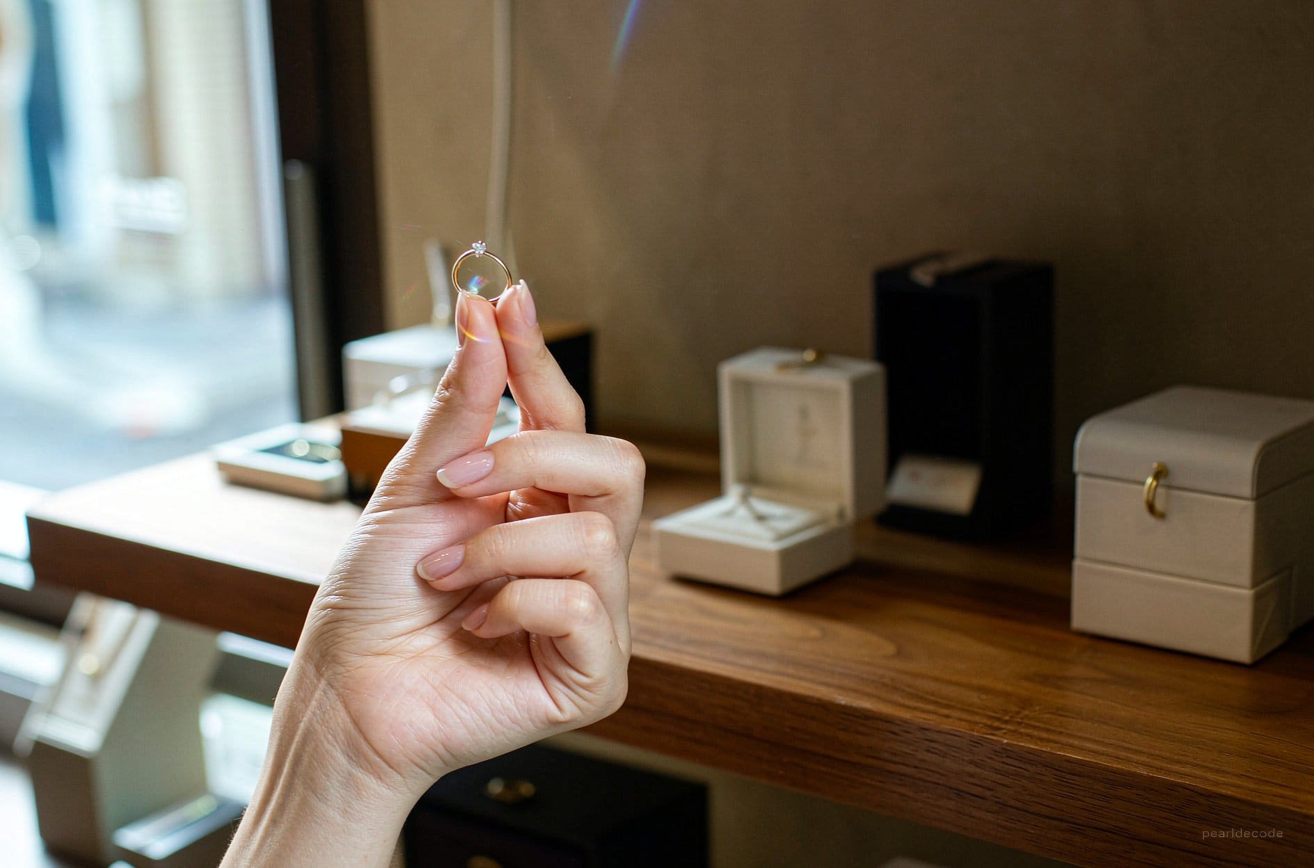 Hand holding a moissanite solitaire ring near open jewelry boxes warm indoor light