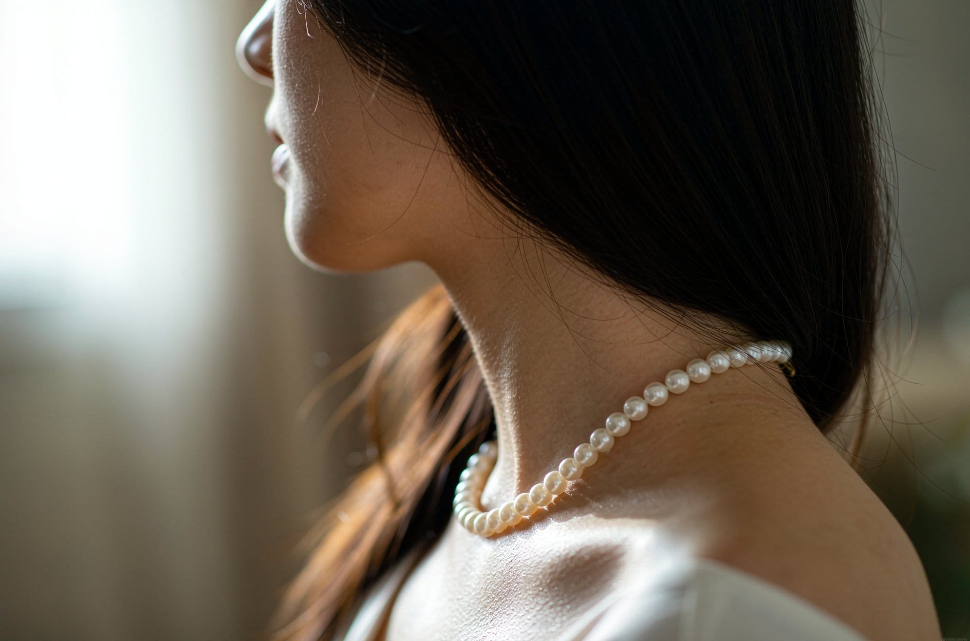 Side profile of a woman wearing a classic pearl strand necklace for pearl vs moissanite guide